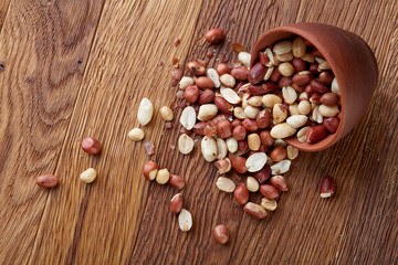 Raw peanuts mix in overturned ceramic bowl isolated over rustic wooden backround, top view, close-up.