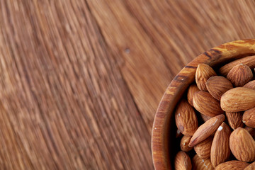 Bowl of almonds on wooden background, top view, close-up, selective focus.