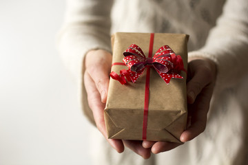 Woman hands holding present with red bow.