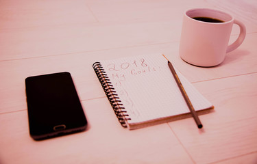 Top view 2018 goals list with phone, cup of coffee and pencil. Business plan.