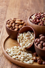 Mixed nuts in brown bowls on wooden tray over rustic background, close-up, top view, selective focus.