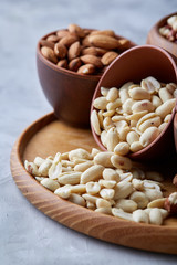 Mixed nuts in brown bowls on wooden tray over white background, close-up, top view, selective focus.