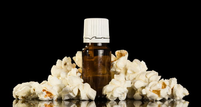 Bottle of aromatic liquid for electronic cigarettes, handful of popcorn nearby, isolated on black
