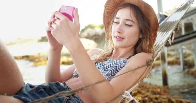 Young woman lying in a hammock texting on her phone
