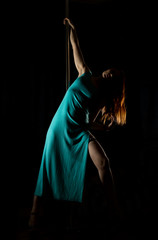 sexy woman pole dancer in a long turquoise dress with a slit on a dark background