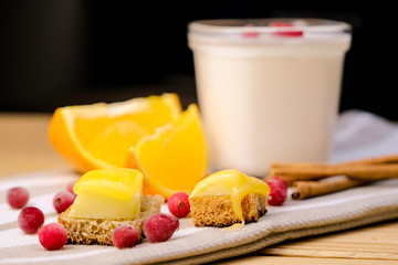 Healthy eating concept: a jar of homemade yoghurt with fresh cranberries, sticks of cinnamon, fresh orange and small sandwiches