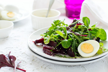 Fresh salad with beetroot, mix leaves, olive oil, egg and sesame seeds on white table cloth