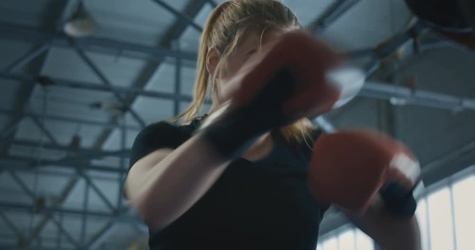 Close view from below of focused athletic woman in boxing gloves working out on technique while training with coach on ring.