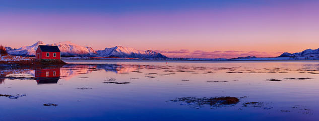 Landscape with beautiful winter lake, red rorbu house and snowy mountains at sunset at Lofoten Islands in Northern Norway. Panoramic view - obrazy, fototapety, plakaty