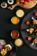 top view of tasty roasted chicken wings with various sauces and vegetables on black