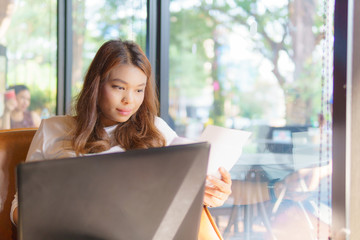 beautiful asian young business woman sitting near transparent window and using laptop for her job at cafe or coffee shop. business concept.
