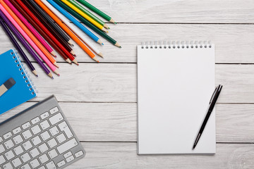 Fototapeta na wymiar White notepad, keyboard, color pencils on a white table