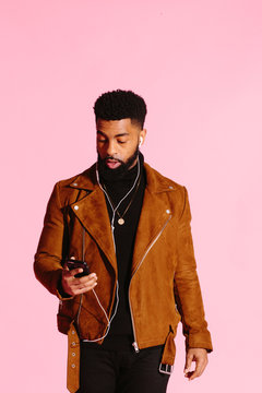 Cool African American man with beard looking down at his phone surprised, isolated on pink studio background