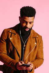 Cool man with beard looking down and texting on his phone , isolated on pink studio background