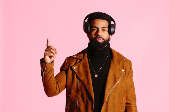 Cool African American man with beard and headphones pointing up, isolated on pink studio background