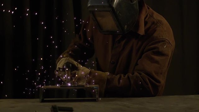 Person welding while slow motion sparks fly and smoke rises.