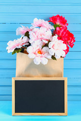 Pink peonies in a craft package with a chalkboard on a blue wooden table. Postcard for the holiday. Copy the space.