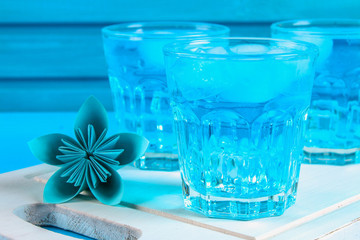 Blue cocktail with ice and mint in glasses on a white wooden board on a blue table.