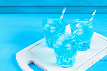 Blue cocktail with ice and mint in glasses on a white wooden board on a blue table.