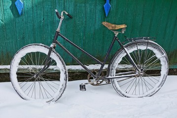 Fototapeta na wymiar Old bicycle in the snow near the green wall