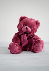 Cute hugable burgundy teddy bear on white wooden table and white background