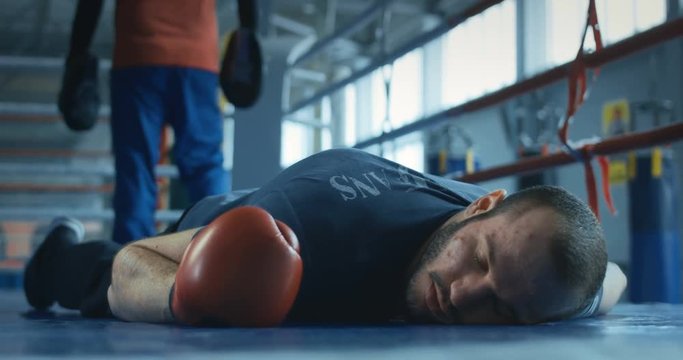 Sportive man in boxing gloves lying in knock-out on ring with eyes closed.