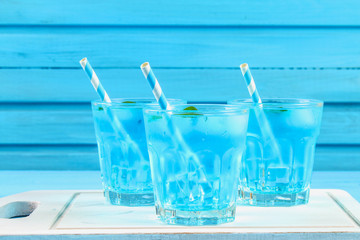 Blue cocktail with ice and mint in glasses on a white wooden board on a blue table.
