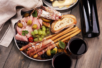 Italian antipasti wine snacks set. Cheese variety, Mediterranean olives, pickles, Prosciutto di Parma, salami and wine in glasses over black grunge background.