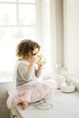 Little girl drinking tea in white kitchen