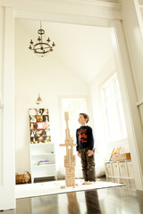 Boy standing tall with wooden block tower