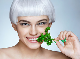 Beautiful smiling girl with parsley. Photo of fashion blonde girl on blue background. Close up. Healthy lifestyle concept