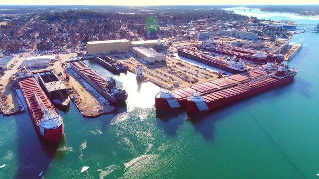 Many large freighter ships docked in ice covered waters, aerial view.
