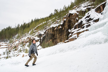 Young man tourist walking on nature of reserve Stolby. On mountaain and ice waterfall background.