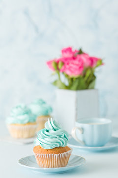 Blue pastel vertical banner with decorated cupcakes, cup of coffe with milk and bouquet of pink roses.