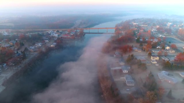 Aerial view of tranquil foggy river through small town USA at sunrise.
