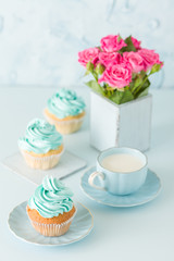 Blue pastel vertical banner with decorated cupcakes, cup of coffe with milk and bouquet of pink roses.