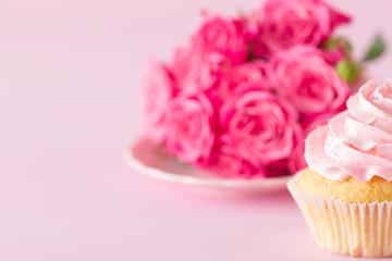 Cupcake with pink cream decoration and roses on pink pastel background.