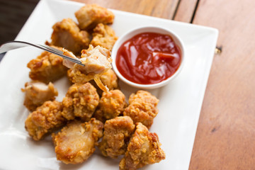 Sliced chicken fried served with ketchup on white plate. Crunchy snack. Favorite fast food. Fork picking ready to eat. Top view with copy space.
