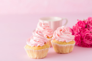 Cupcake with pink cream decoration and roses on pink pastel background.