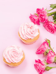 Cupcake with pink cream decoration and roses on pink pastel background.