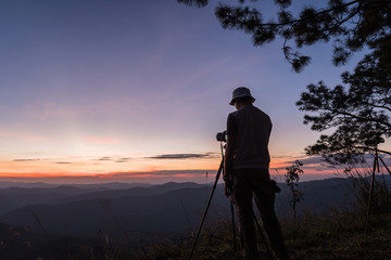 Hiker with camera on tripod takes picture from rocky summit.