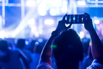 Crowd of hands up concert stage lights enjoying concert, and man use smartphone for record clip of people fan audience silhouette raising hands in festival music rear view spotlight glowing, blurred