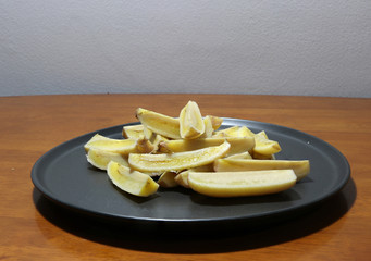Cultivated banana boiled and cut into pieces in the black dish on the wooden table.