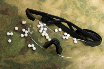 balls airsoft bbs and protective glasses on a camouflage background