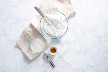 Overhead of powdered sugar in glass bowl with wire whisk and cream, cinnamon and silver tablespoon.