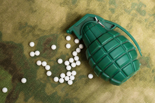 airsoft bbs balls and toy grenade on camouflage background