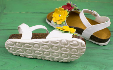 sandals for children with flowers on a green wooden surface