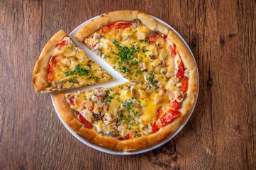 A triangular piece of pizza is separated..Home made pizza on white plate dish on dark oak wood table