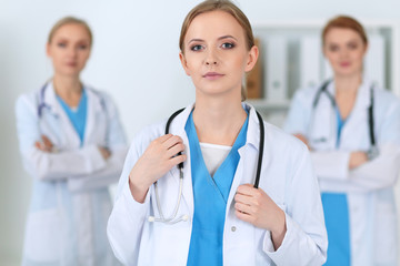 Beautiful female medical doctor standing at hospital in front of medical group. Physician is ready to help patients. Medicine and health care concept