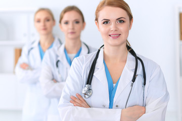 Beautiful female medical doctor standing at hospital in front of medical group. Physician is ready to help patients. Medicine and health care concept